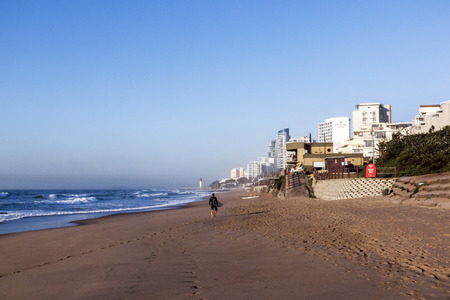 UMHLANGA, DURBAN, SOUTH AFRICA - JULY 8, 2016: One unknown male surfer on early morning beach against commercial and residential complexes in Umhlanga Rocksのeditorial素材