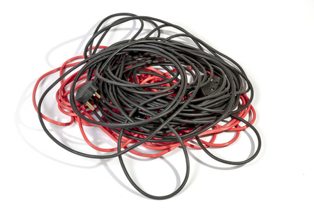 Studio shot of untidy pile of rolled red and black electric extension cables on white background