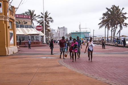 DURBAN, SOUTH AFRICA - OCTOBER 30, 2016: Many unknown people walking along  paved promenade at North Beach on Golden Mile beachfront on overcast wet afternoon in Durbanのeditorial素材