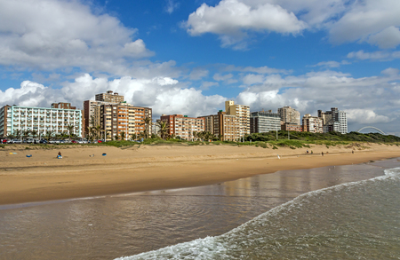 DURBAN, SOUTH AFRICA - DECEMBER 2, 2016: Few unknown early morning visitors and  calm sea against blue cloudy sky and golden mile city skyline in Durbanのeditorial素材