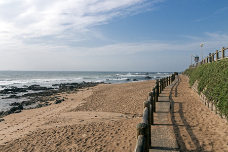 Retaining wall and wooden barrier on  empty beach against blue skyline and residential buildings on beach in Ballito near Durban, South Africaの写真素材