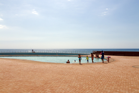 SCOTTBURGH, DURBAN, SOUTH AFRICA - DECEMBER 23, 2016: Many unknown adults and children at seaside swimming pool against ocean and skyline at Scottburgh beach near Durban, South Africaのeditorial素材