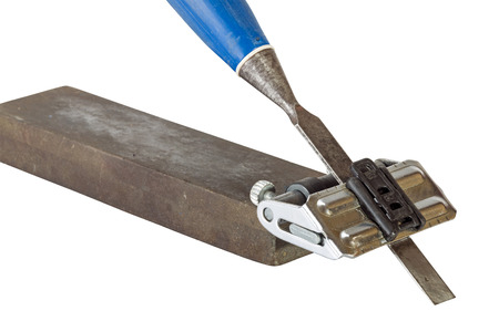 Close up studio shot of chisel clamped in angle guide jig resting on grinding whetstones on white...