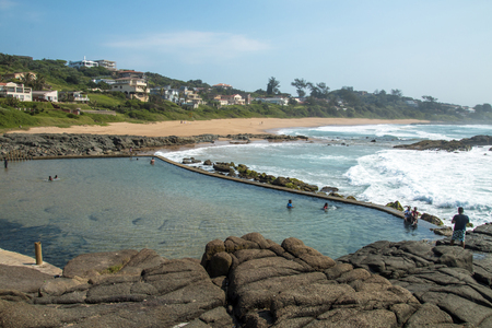 TINLEY MANOR, DURBAN, SOUTH AFRICA - FEBRUARY12 , 2017: Many unknown people at early morning Tinley Manor tidal pool against beach and coastal residential building landscape north of Durban in South Africaのeditorial素材