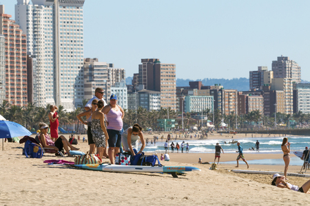 DURBAN, SOUTH AFRICA ; APRIL 24, 2017: Many unknown people on morning visit to beach against Durban city skyline in South Africaのeditorial素材