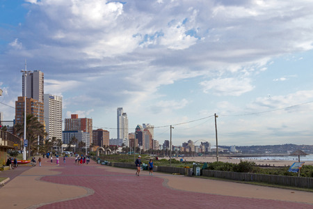 DURBAN, SOUTH AFRICA - SEPTEMBER 1, 2017: Many unknown people on early morning  paved promenade on beachfront against cloudy city skyline landscape in Durban, South Africaのeditorial素材