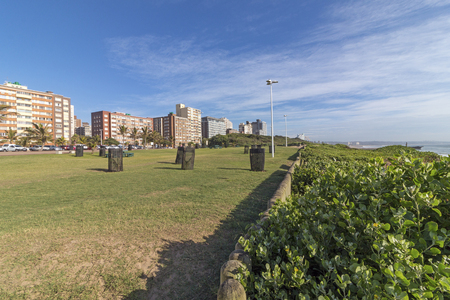 Empty grass verge wooden poled barrier with dune vegetation and sea against distant Durban city blue cloudy skyline coastal landscape in South Africaの写真素材