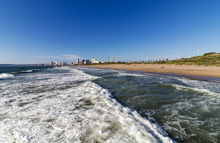 Coastal landscape of waves breaking on beach against blue city skyline in Durban, South Africaの写真素材