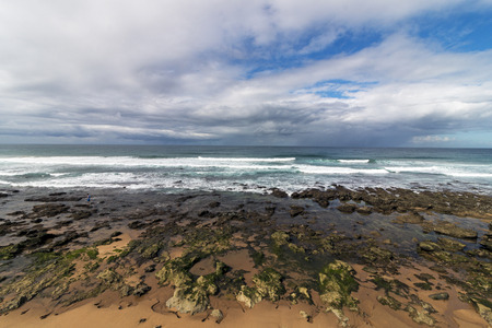 Low tide rocky beach waves and ocean against blue cloudy sky seascape in Durban, South Africa