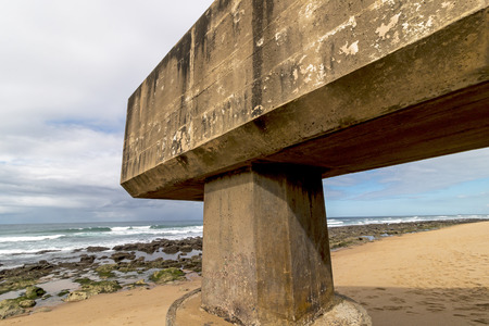 Concrete drainage pipeline extending onto sandy beach against rocky shoreline and blue cloudy coastal landscape at Garvies beach on the Bluff,  Durban, South Africaの写真素材
