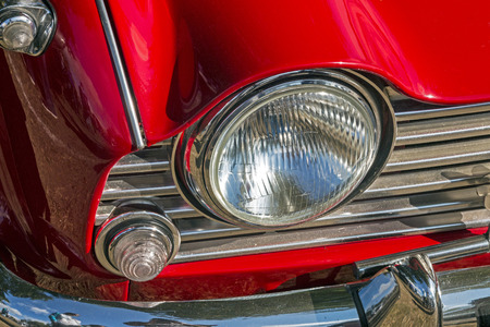 Close uo of vintage red vehicle right front light grill, chrome bumper and red bonnetの写真素材