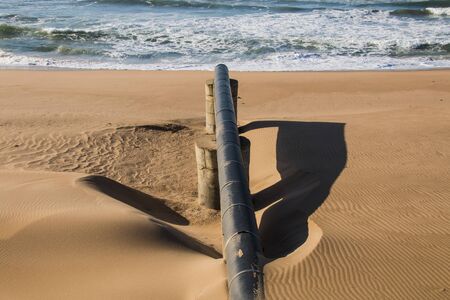 Exposed long black pipe leading into sea at low tide on coastlineの写真素材