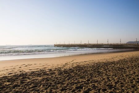 Stretch of beach with lenghty pier and bluff in distanceの写真素材