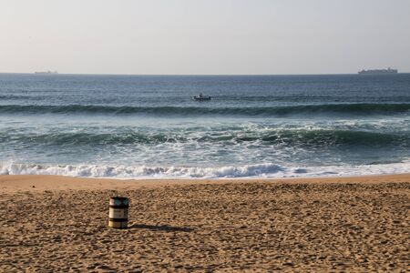 Footprints on the shoreline with a garbage bin and ships at sea
