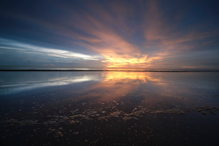 Sunset on the beach at low tide with reflection in water.の写真素材