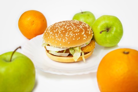 chicken burger next to many apples and orangesの写真素材