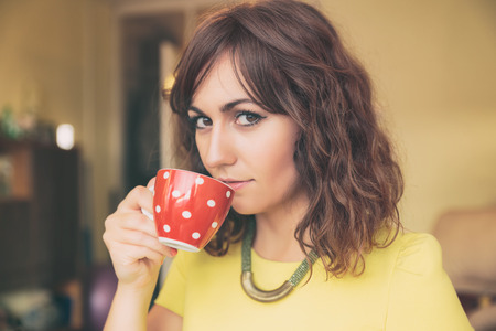 Close Up of Woman Drinking from Red Polka Dot Tea Mug and Looking at Cameraの写真素材