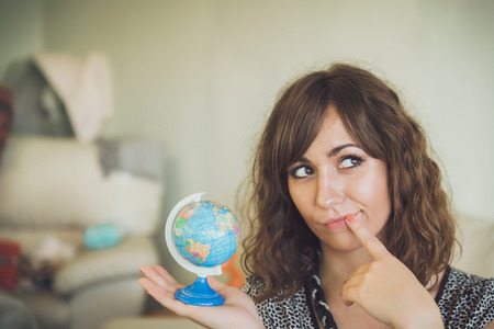 Thinking Woman Holding Small Globe in Hand as if Deciding Where to Travelの写真素材