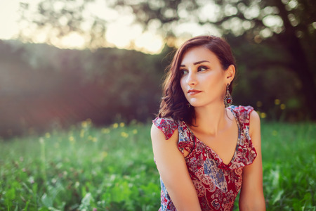Macro Pretty Young Woman in Floral Maroon Dress on Grassy Fieldの写真素材