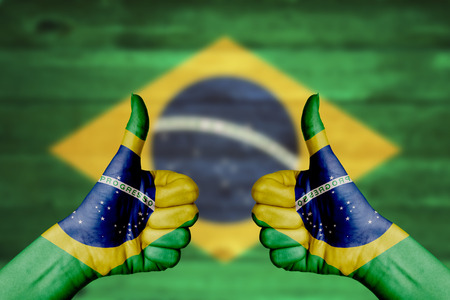 Brazil flag painted on female hands thumbs up with blurry wooden backgroundの写真素材