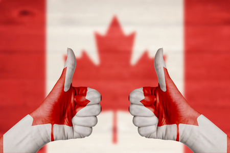 Canada flag painted on female hands thumbs up with blurry wooden backgroundの写真素材