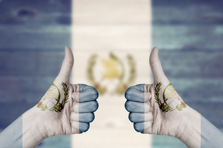 Guatemala flag painted on female hands thumbs up with blurry wooden backgroundの写真素材