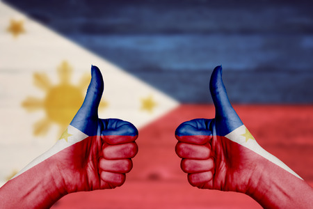 Philippines flag painted on female hands thumbs up with blurry wooden backgroundの写真素材