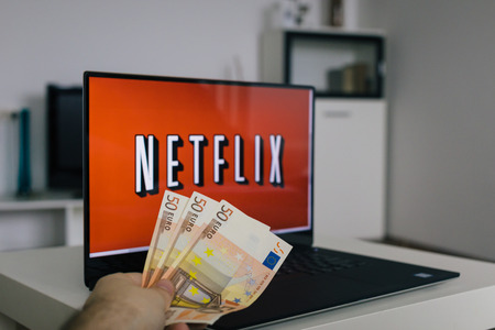 Zagreb, Croatia - December 20, 2015: Netflix on laptop screen, man throwing Euro bills at it. Netflix is an international provider of on-demand Internet streaming media.のeditorial素材