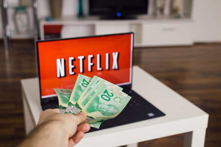 Zagreb, Croatia - December 20, 2015: Netflix on laptop screen, man throwing Canadian dollars at it. Netflix is an international provider of on-demand Internet streaming media.のeditorial素材