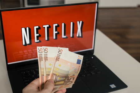 Zagreb, Croatia - December 20, 2015: Netflix on laptop screen, man throwing Euro bills at it. Netflix is an international provider of on-demand Internet streaming media.のeditorial素材