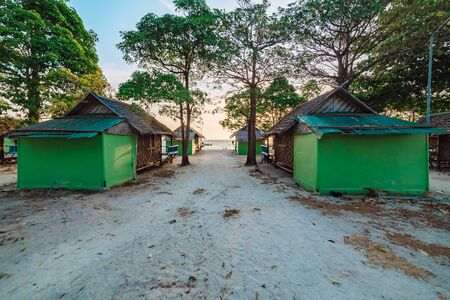 Cabana beach huts on a sandy beach Koh Lipe, Thailand with the glow of the rising sun behind leafy green trees in a scenic tropical landscapeの写真素材