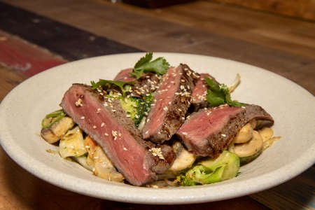 A delicious plate of beef satay stir fry steak packed full of vegetables and topped with seeds on a white plateの写真素材