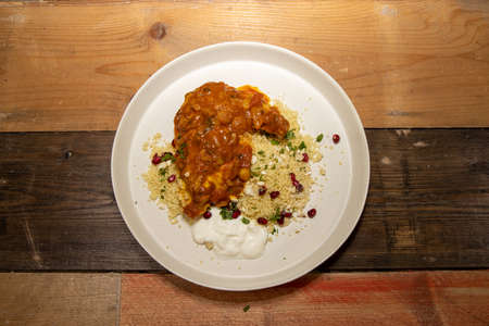 A delicious plate of slow cooked melt in the mouth Chicken Tagine, with couscous and pomegranate on a rustic wooden kitchen work top.の写真素材