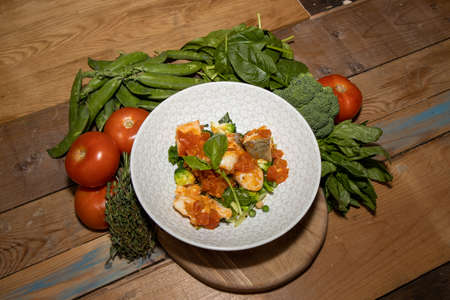 A delicious bowl of Sea food tomato and Vanilla Stew in a white bowl surrounded by the ingredients used to create the fish dish on a wooden kitchen tableの写真素材