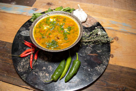 A delicious bowl of minestrone soup with dumplings on a wooden kitchen work top surrounded by peppers, garlic and herbsの写真素材