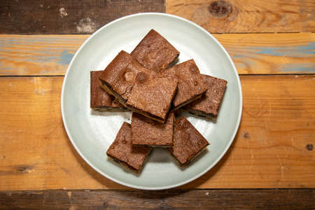 A plate of delicious chocolate brownies on a wooden kitchen work top, tasty deserts in a pile ready to be eatenの写真素材