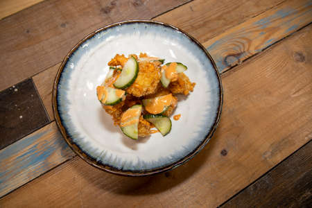 A delicious plate of fried chicken with chilli mayonnaise mayo and cucumber slices on a wooden kitchen work topの写真素材