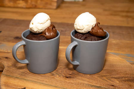 A cup of chocolate cake that has been made in a microwave with chocolate source and ice cream on a...