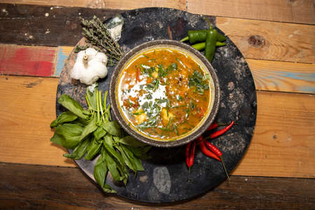 A delicious bowl of minestrone soup with dumplings on a wooden kitchen work top surrounded by...