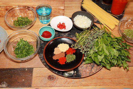Ingredients for spaghetti bolognese in a kitchen on a wooden worktop showing spices, herbs, coriander, onions and dried spaghetti, food preparation conceptの写真素材