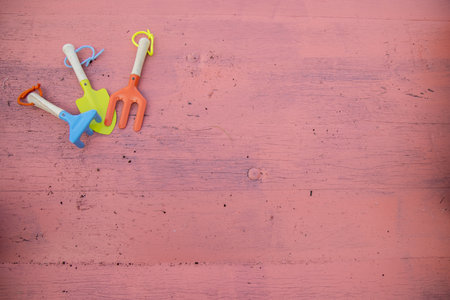 A set of children's small gardening tools including a spade, digger and rake on a pink wooden backgroundの写真素材