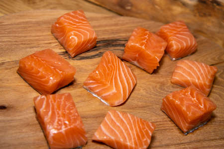 Diced sliced cubes of pink salmon fish on a wooden work top chopping board