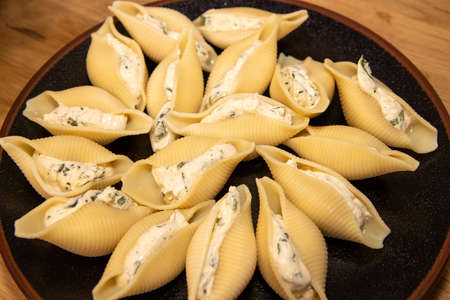 A plate of delicious Spinach & Ricotta pasta shells on a wooden kitchen work top, ready to be put in the ovenの写真素材