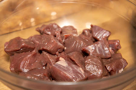 A bowl of uncooked raw venison meat in a glass bowl on a wooden kitchen work topの写真素材