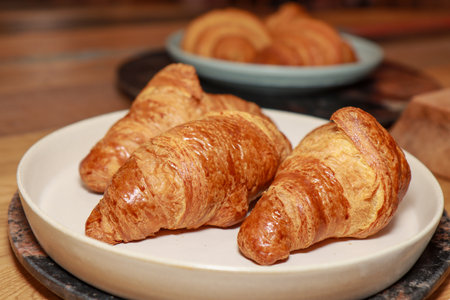 A plate of three freshly made croissants on a plate in a kitchen on a wooden work topの写真素材