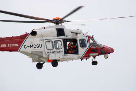 East Sussex, Beachy Head, UK 10th July 2019: The HM Coastguard Rescue Helicopter attending an incident on the Beachy Head cliffs flying in the sky on a bright cloudy day over the ocean.のeditorial素材