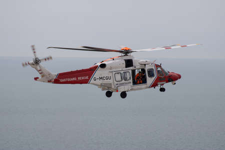 East Sussex, Beachy Head, UK 10th July 2019: The HM Coastguard Rescue Helicopter attending an incident on the Beachy Head cliffs flying in the sky on a bright cloudy day over the ocean.のeditorial素材