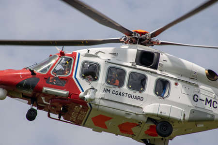 East Sussex, Beachy Head, UK 10th July 2019: The HM Coastguard Rescue Helicopter attending an incident on the Beachy Head cliffs flying in the sky on a bright cloudy day over the ocean.のeditorial素材