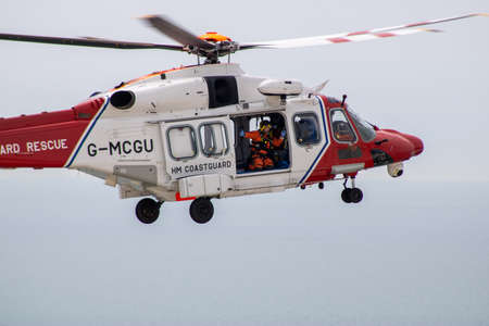 East Sussex, Beachy Head, UK 10th July 2019: The HM Coastguard Rescue Helicopter attending an incident on the Beachy Head cliffs flying in the sky on a bright cloudy day over the ocean.のeditorial素材