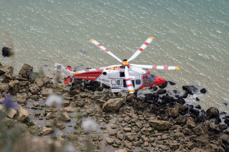East Sussex, Beachy Head, UK 10th July 2019: The HM Coastguard Rescue Helicopter attending an incident on the Beachy Head cliffs flying in the sky on a bright cloudy day over the ocean.のeditorial素材